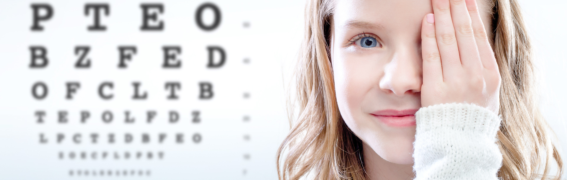Young girl covering her left eye with an eye chart in the background